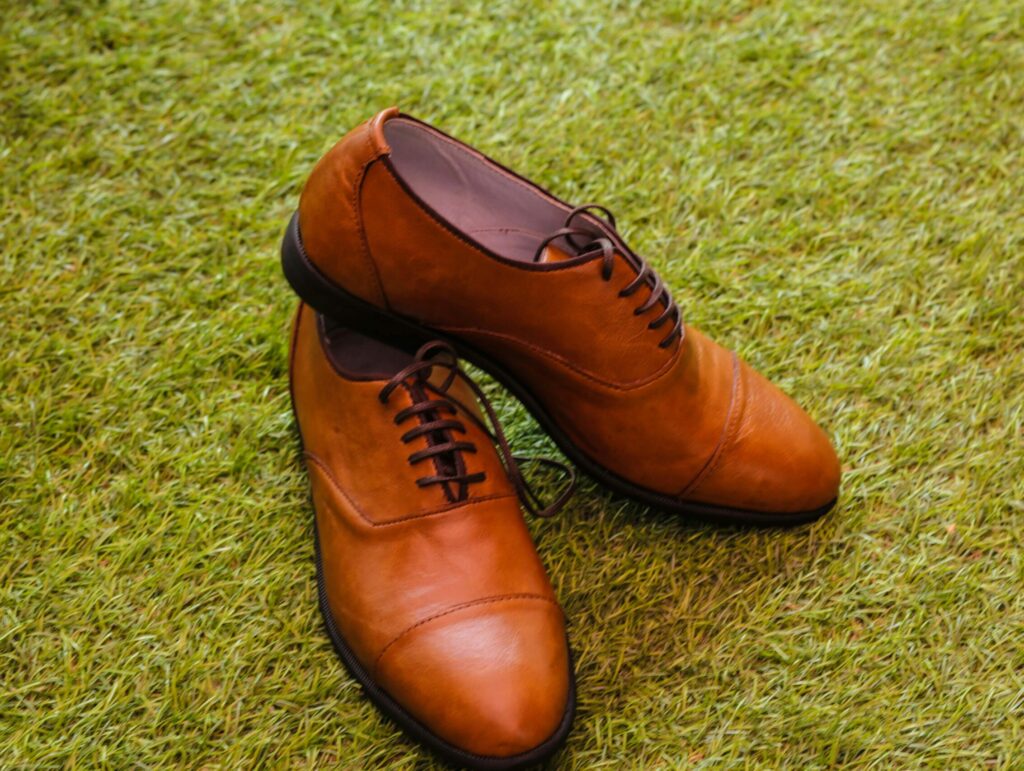 A stylish pair of brown leather oxford shoes elegantly placed on lush green grass.