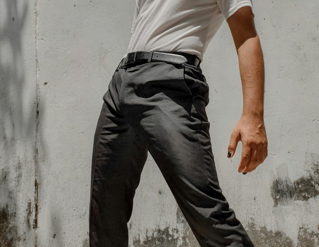 A stylish young man striking a confident pose against a rustic white wall outdoors.